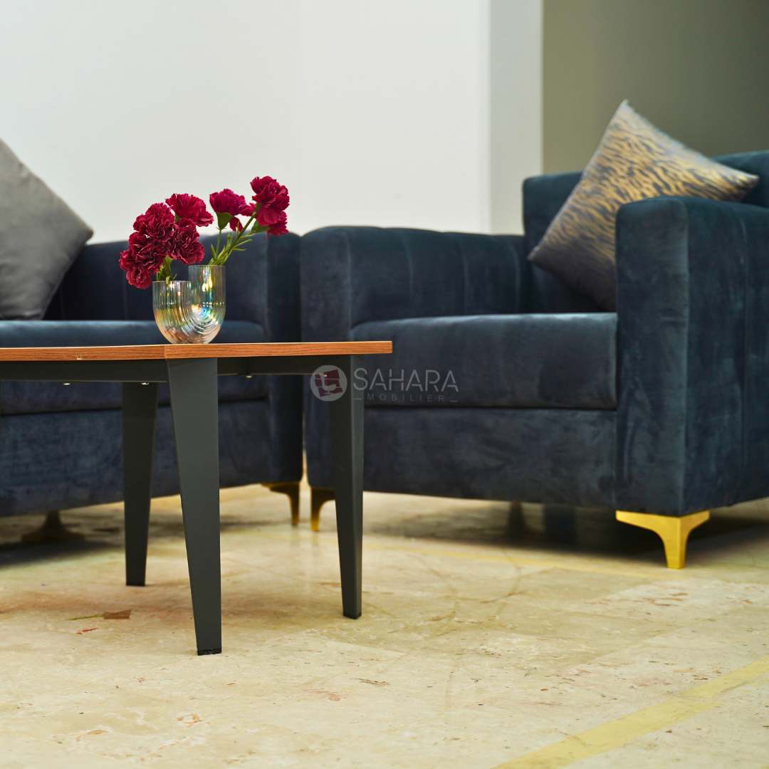 canapé fauteuil en velours en bleu nuit avec des petit coussins carré exposé avec une table en bois