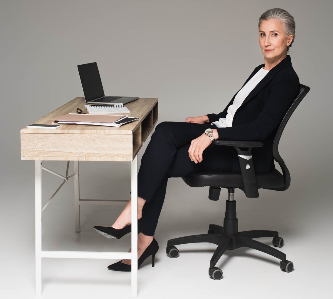 Mature businesswoman sitting near gadgets and papers on table on grey background