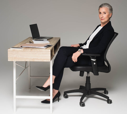Mature businesswoman sitting near gadgets and papers on table on grey background