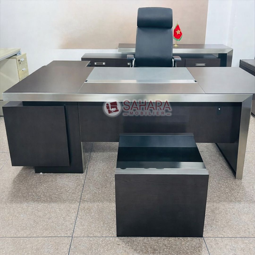 Ce bureau de direction Sahara Mobilier se distingue par son design contemporain, ses lignes droites et son alliance harmonieuse entre MDF haut de gamme et finitions métalliques. Conçu pour les bureaux de direction, cabinets professionnels et administrations, il offre une image de prestige et de sérieux.

Son plan de travail spacieux assure un confort optimal au quotidien, tandis que la structure solide en MDF garantit stabilité et durabilité. Le voile de fond améliore l’ergonomie et l’esthétique, et le pass